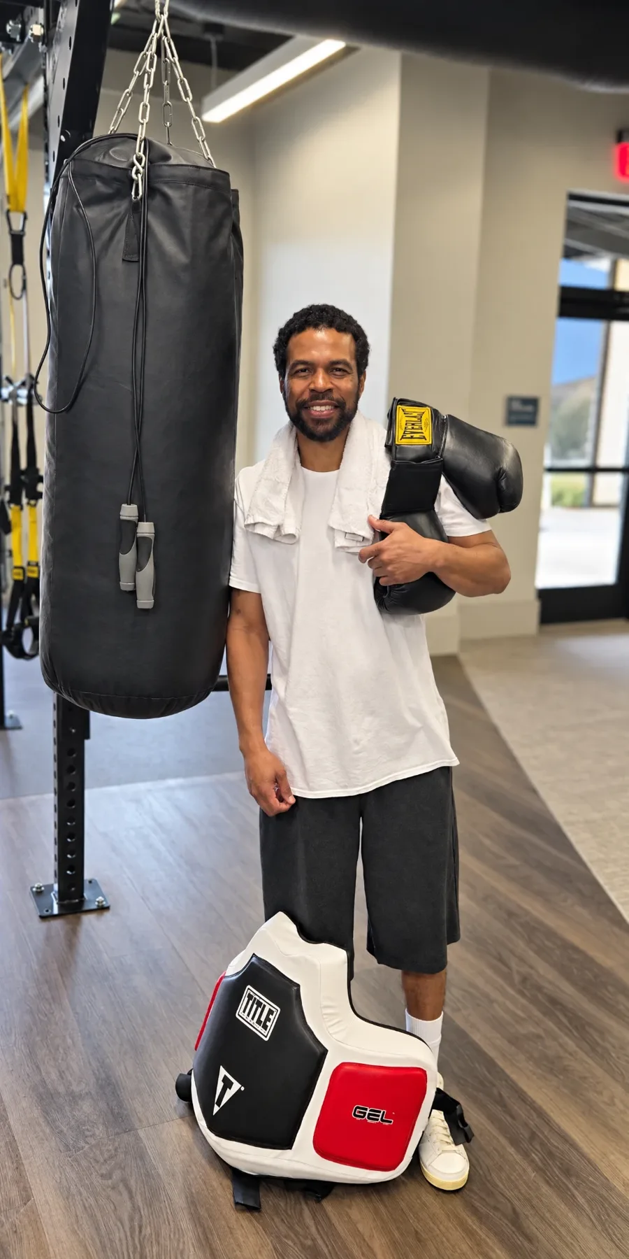 Coach Maurice Cleveland in the gym, holding boxing gloves, standing beside a heavy bag